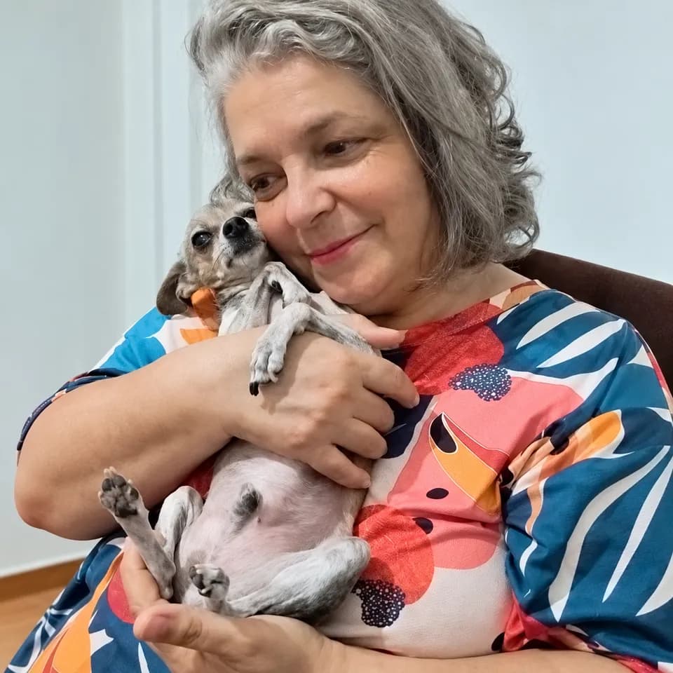Cuidadora do Abrigo da Sih abraçando um cachorro pequeno junto ao rosto.