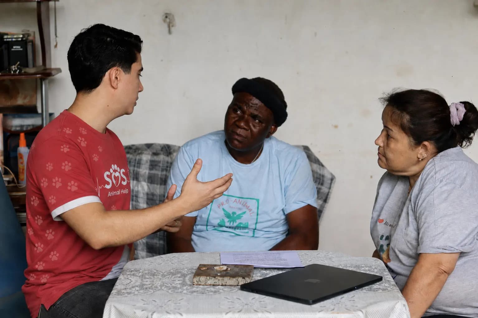 Voluntário da SOS Animal Help explicando os termos do apoio a duas protetoras sentadas à mesa.